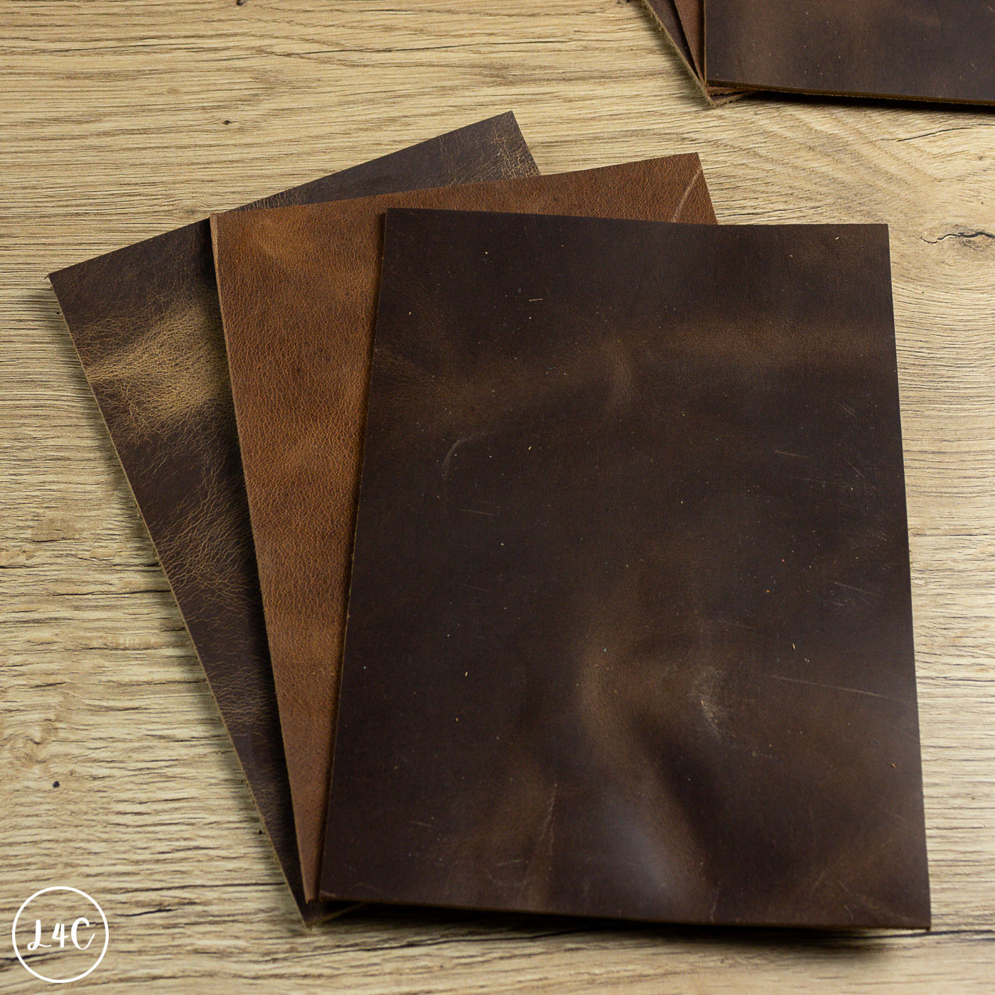 Three pieces of dark brown leather on a wooden surface with Leather4Craft branding.
