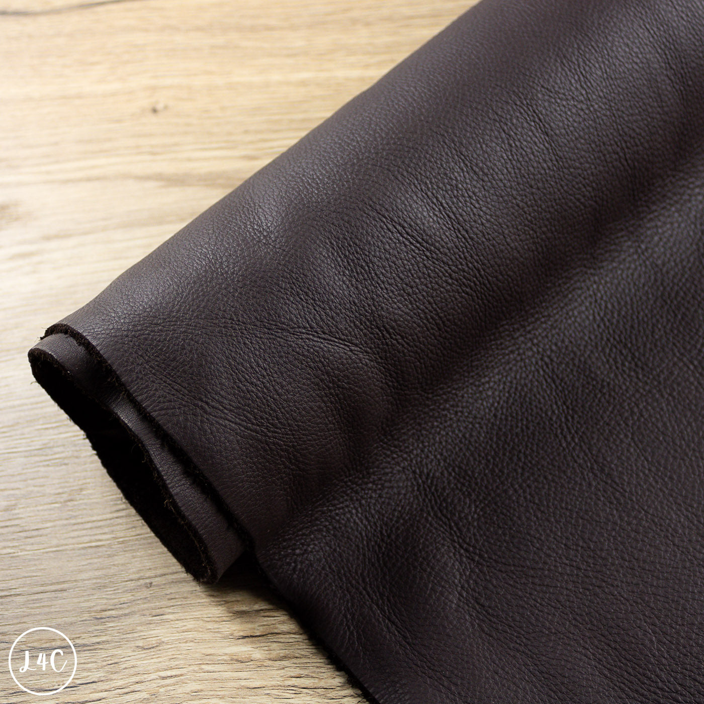 Roll of dark brown leather on a wooden surface
