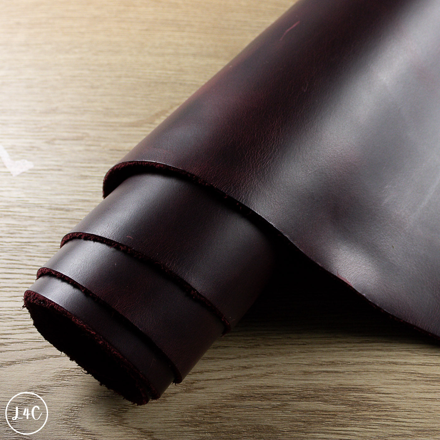 Roll of dark red leather on a light wooden surface