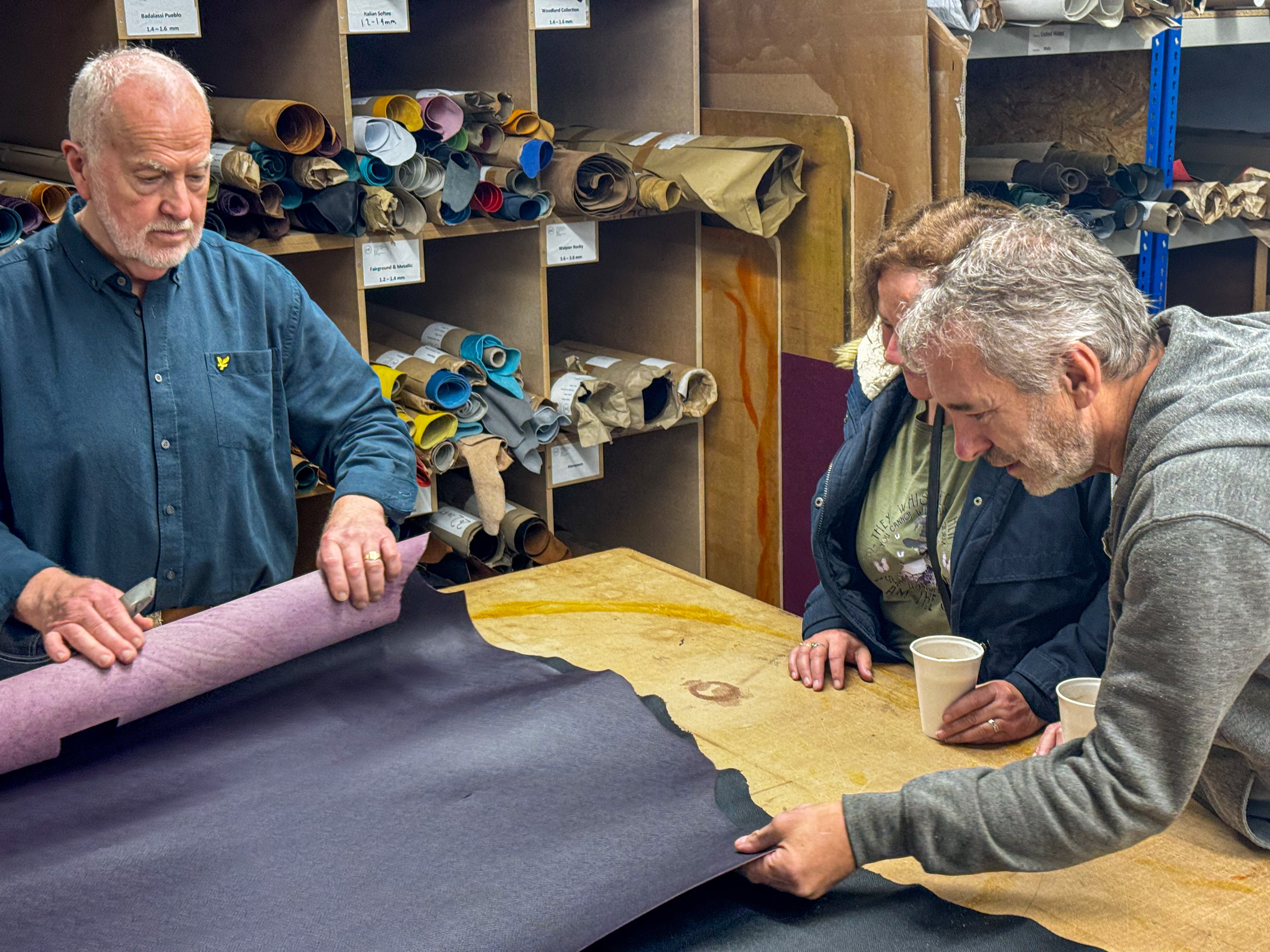 Three men examining leather in a workshop setting.