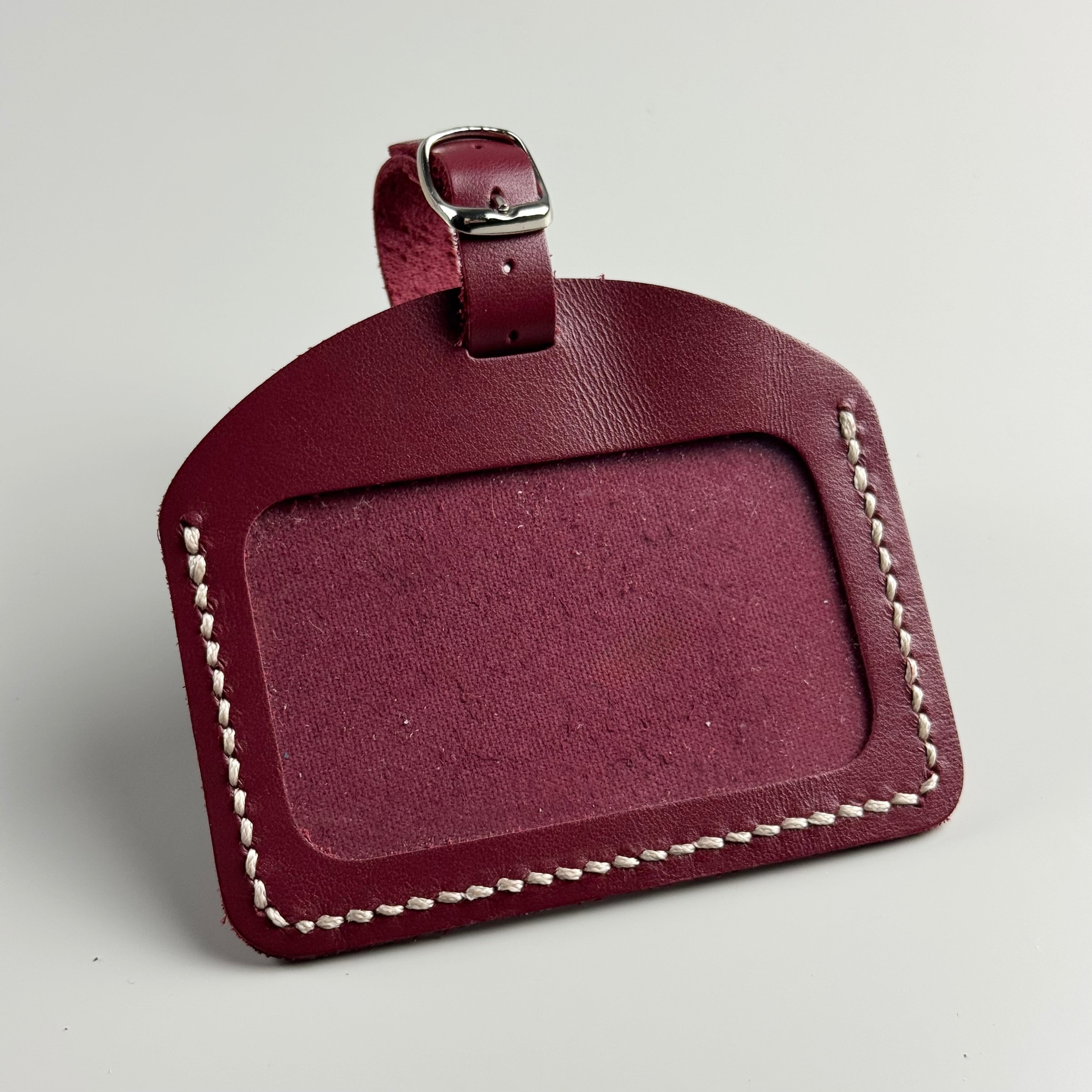 Maroon leather luggage tag with white stitching on a light gray background