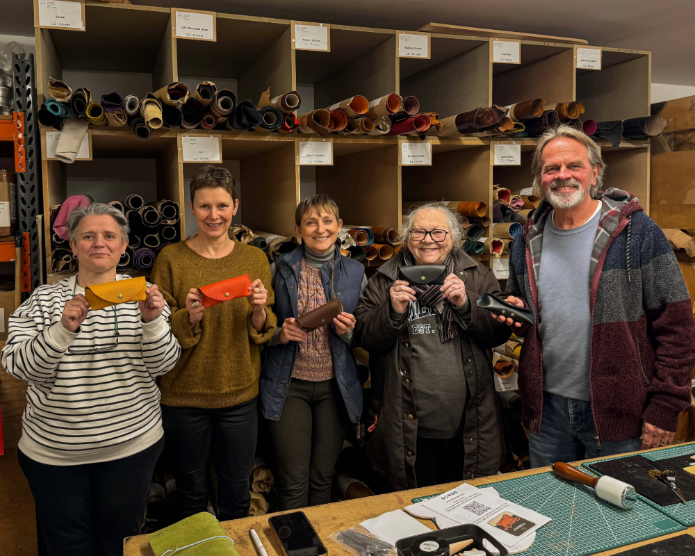 Group of people holding leather pieces in a workshop setting