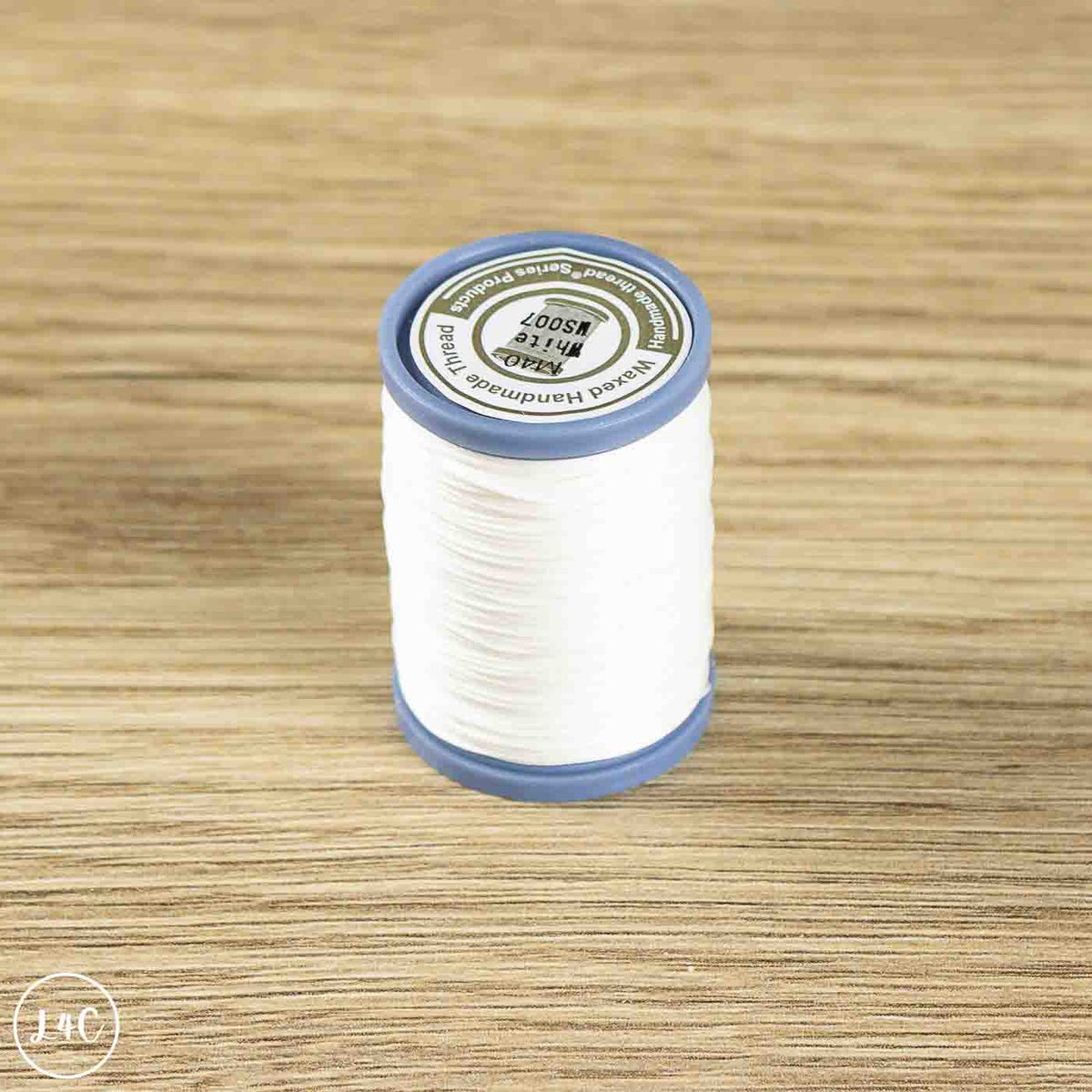 A spool of white sewing thread with blue plastic ends and a white label, placed on a light brown wood-grain surface.