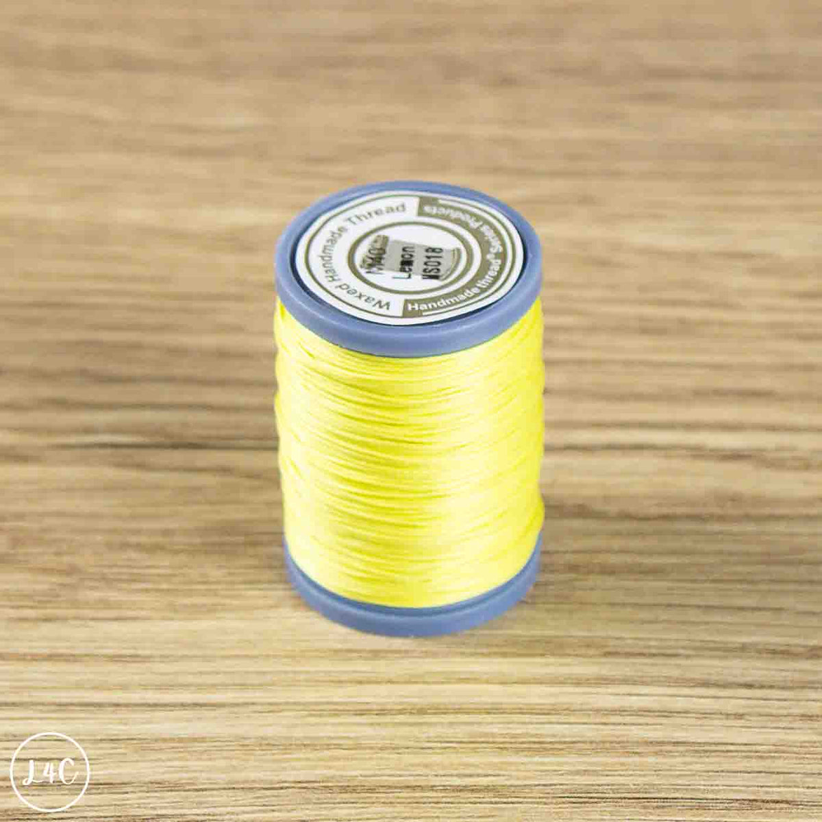 A spool of bright yellow sewing thread with blue plastic ends and a white label, placed on a light brown wood-grain surface.