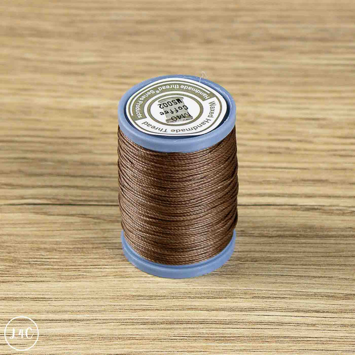 A spool of brown thread labeled 'PMS 4002 Coffee' resting on a light wood grain surface.