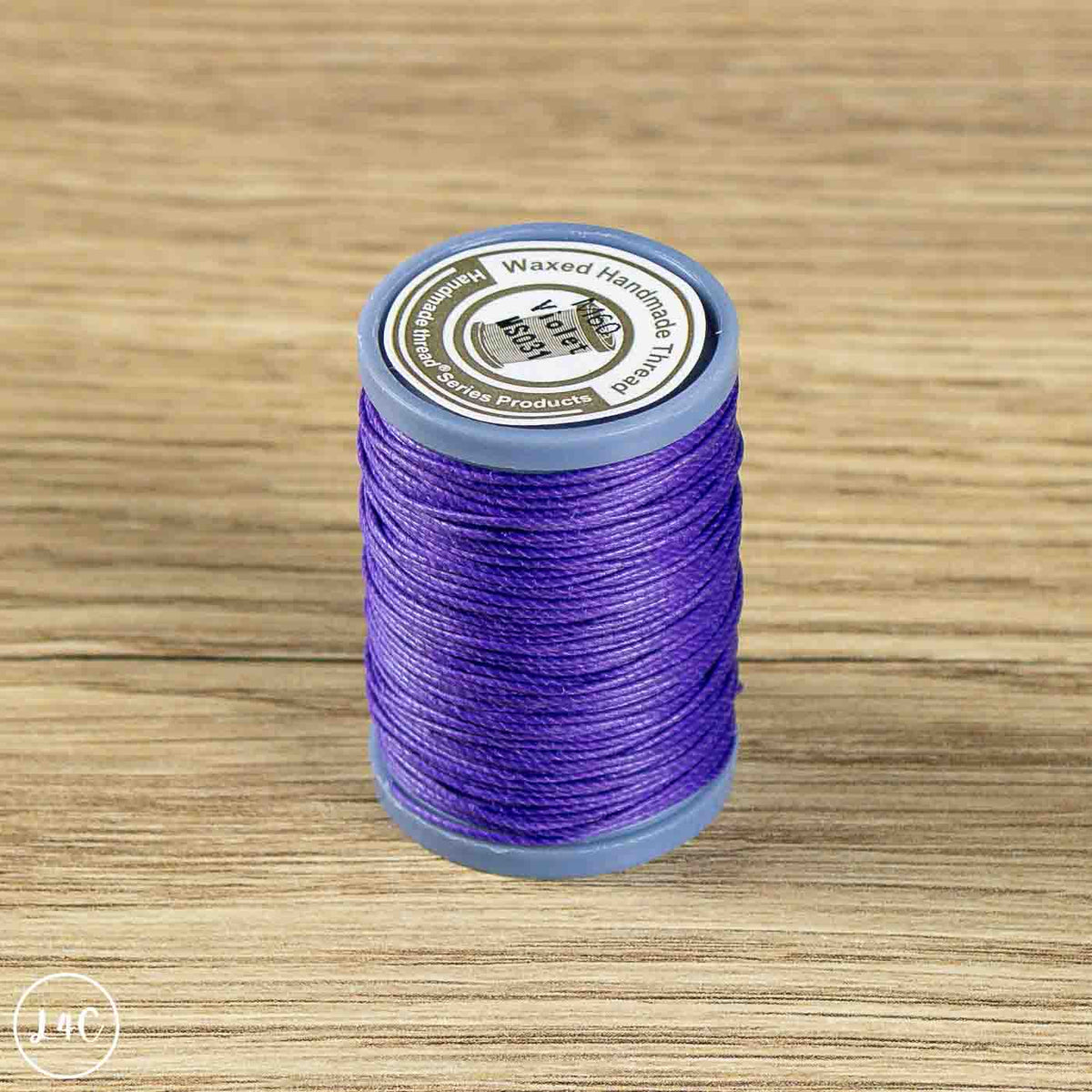 A spool of purple waxed embroidery thread on a light wood grain background. The spool has a blue-gray plastic core.