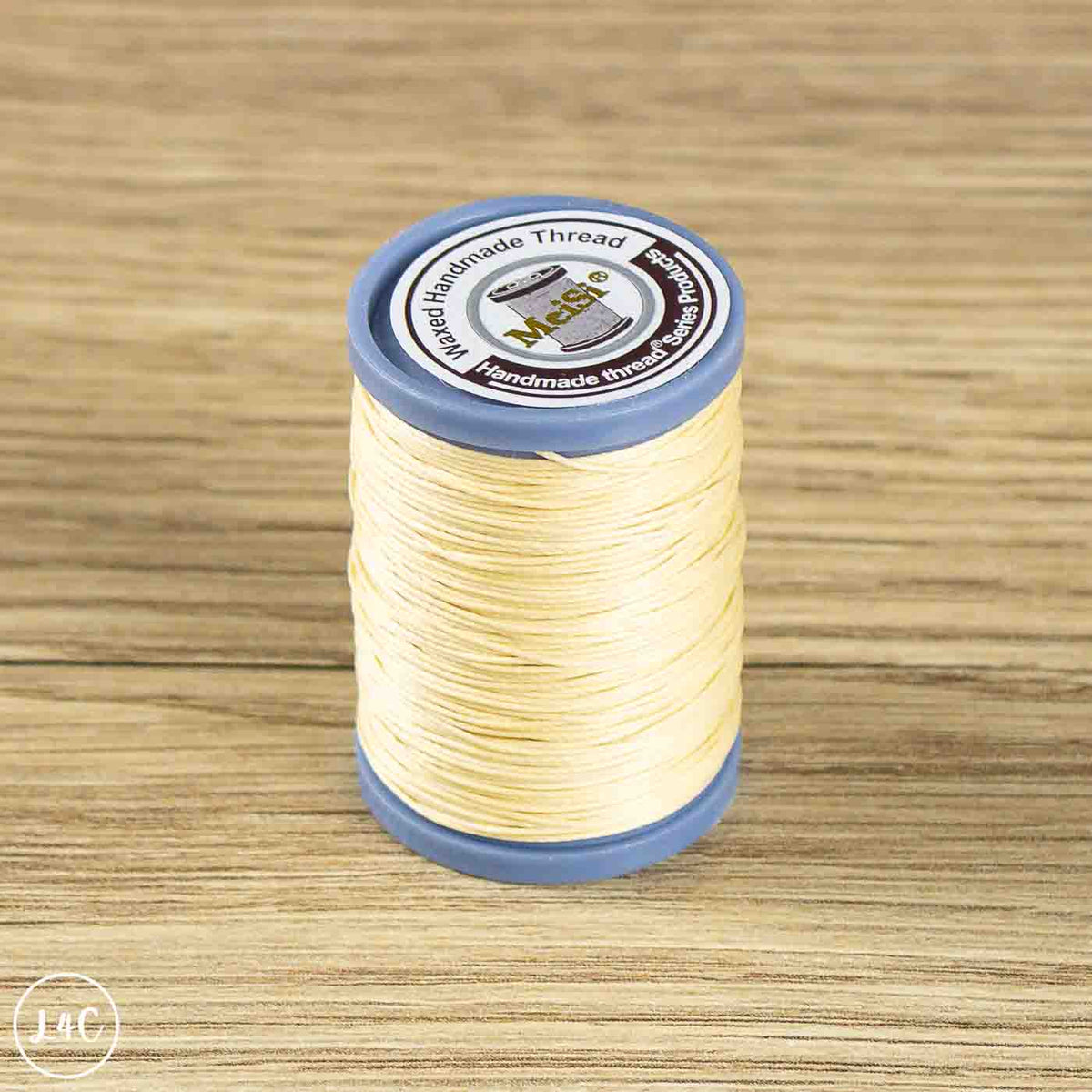 A spool of light beige sewing thread wound on a blue plastic core, placed on a light brown wood-grain surface.