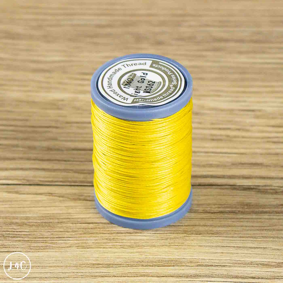 A spool of bright yellow sewing thread wound on a blue plastic cone, placed on a light brown wooden surface.