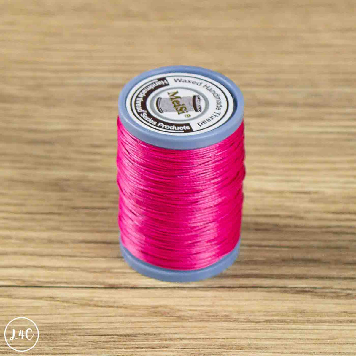 A spool of bright pink sewing thread on a gray plastic core, placed on a light brown wood-grain surface. The top label shows the brand name 'M-A-Size'.