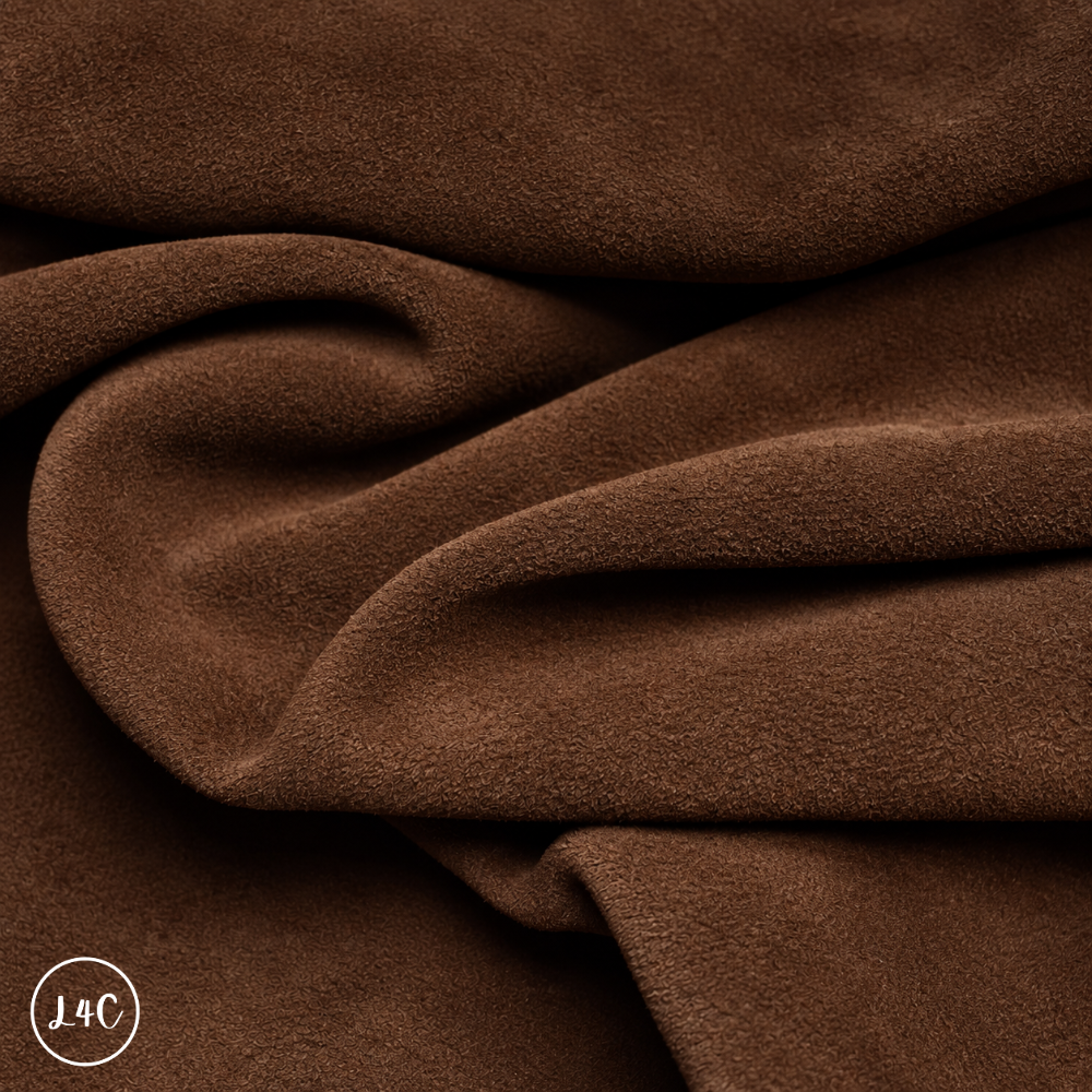 A close-up of draped chocolate brown suede leather with a soft, plush texture, showing deep folds and shadows.