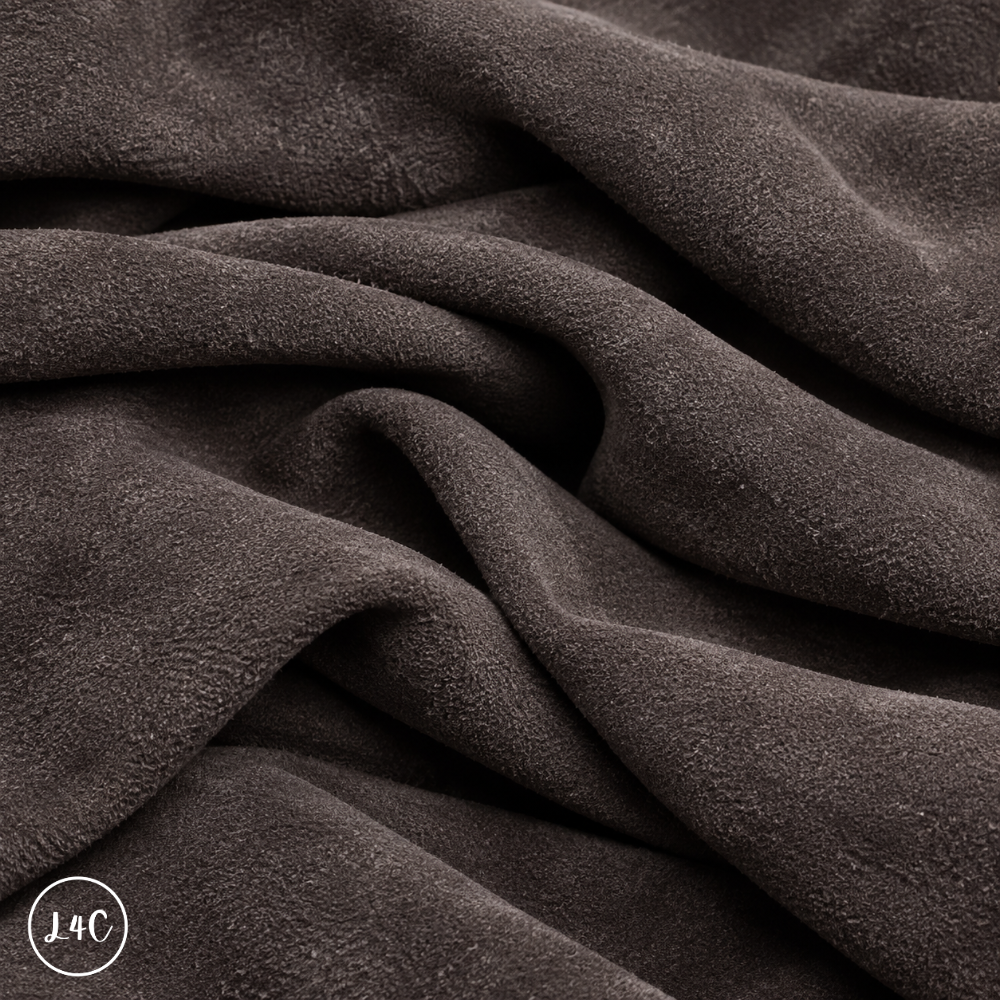 A close-up of draped dark suede leather with a soft, plush texture, showing deep folds and shadows.