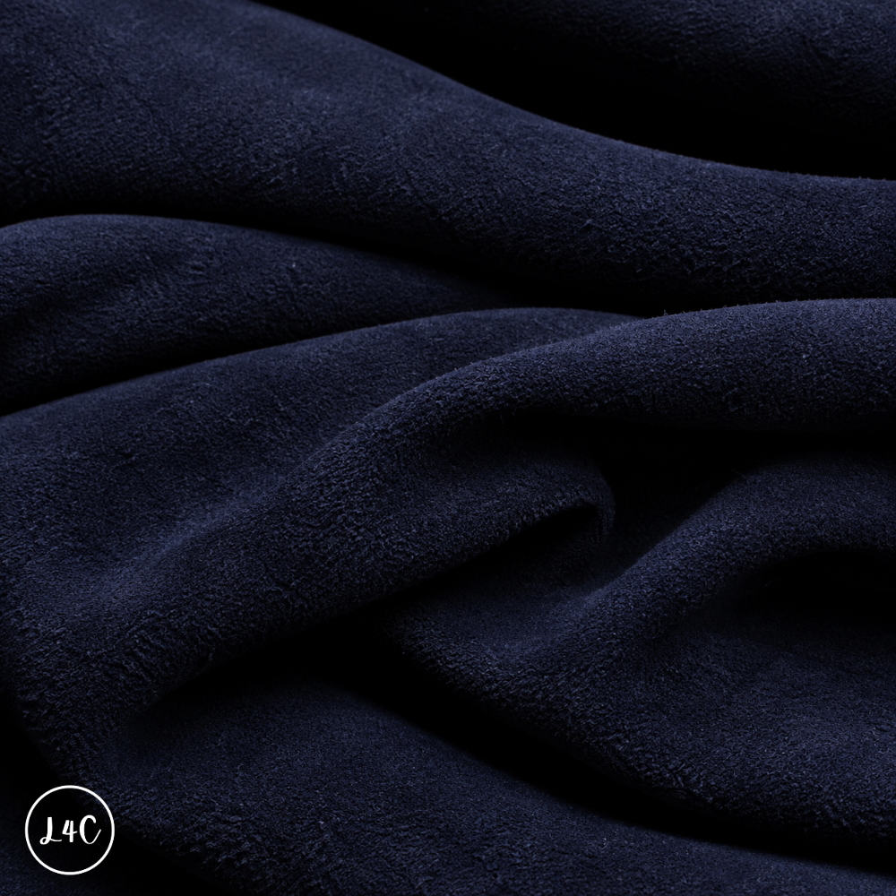 A close-up of draped navy suede leather with a soft, plush texture, showing deep folds and shadows.