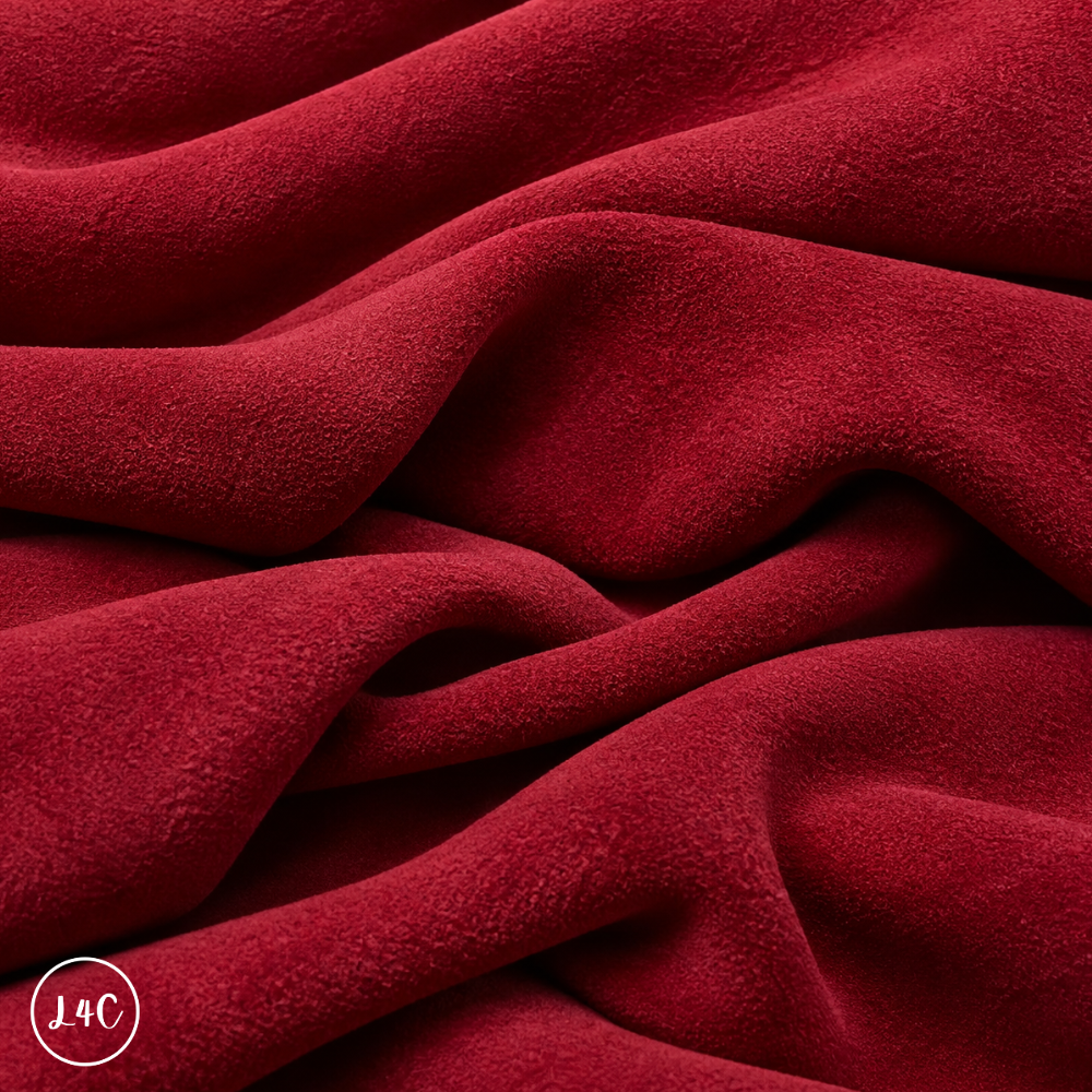 A close-up of draped red suede leather with a soft, plush texture, showing deep folds and shadows.