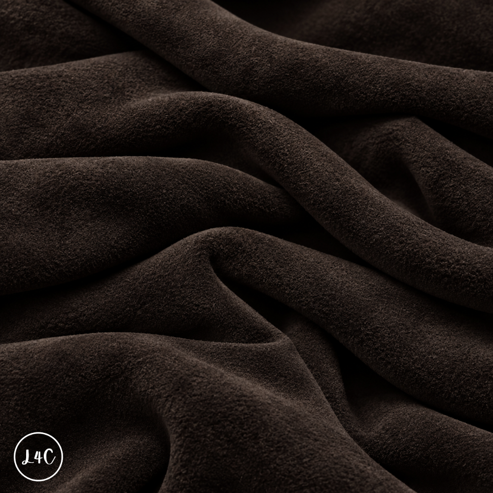 A close-up of draped dark brown suede leather with a soft, plush texture, showing deep folds and shadows.