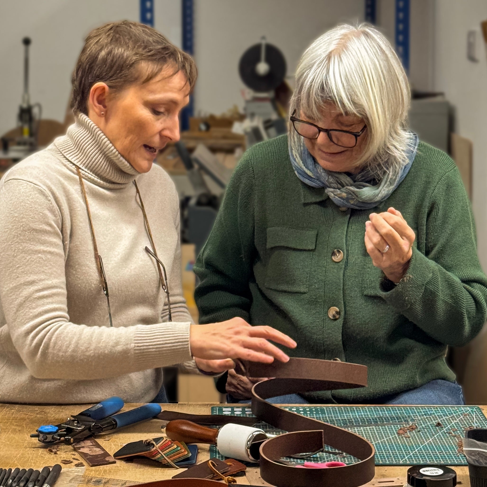 Two women working together on a craft project with tools and materials on a table.