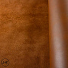 Close-up of brown leather texture with a visible brand logo in the corner showing consistent nap