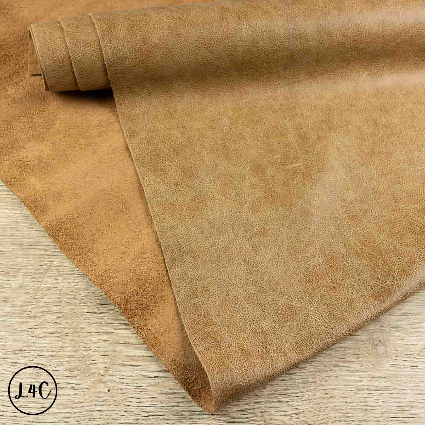 A roll of tan textured leather laid out on a light wood surface, with the material draped diagonally across the frame.