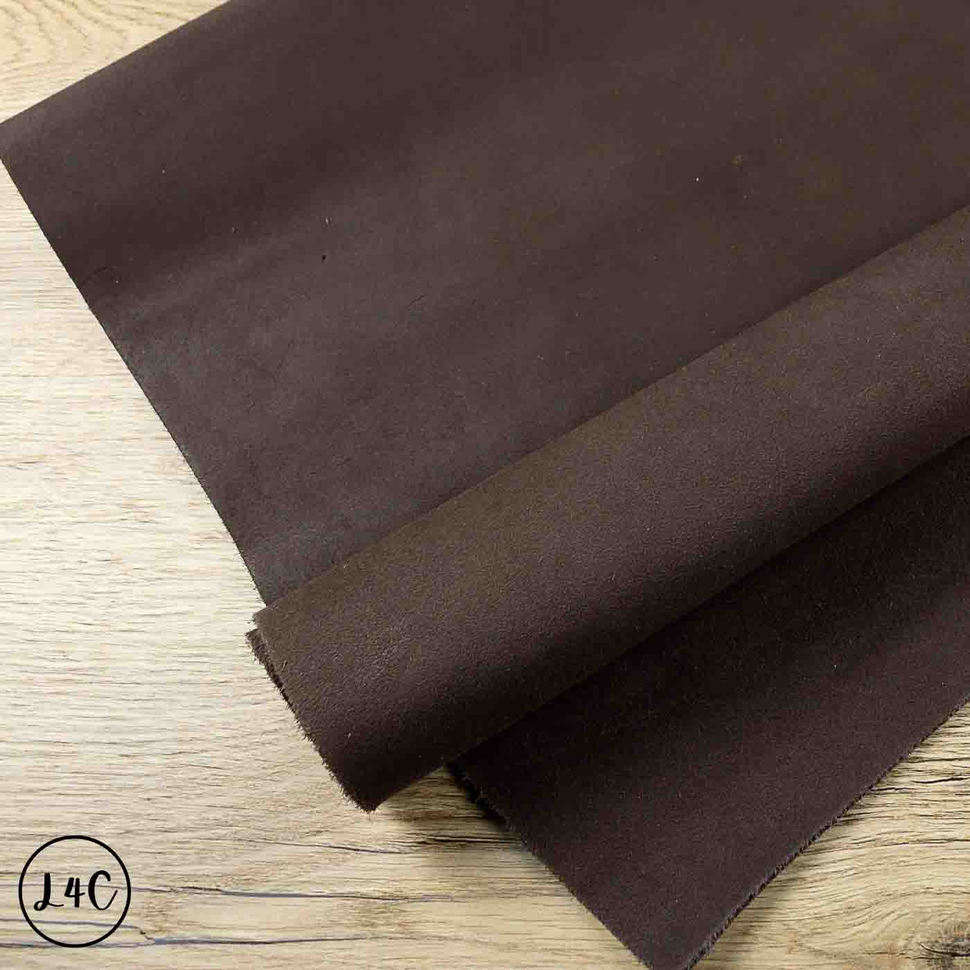 A dark brown suede leather hide roll laid diagonally on a light wood grain surface.