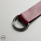 Close-up of a red leather belt with a silver buckle on a light gray background