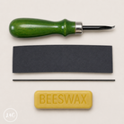 Green leather tool, black leather sample, and bar of beeswax on a beige background