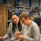 Two women collaborating in a leather workshop, with one holding a piece of orange leather and a small tool. 
