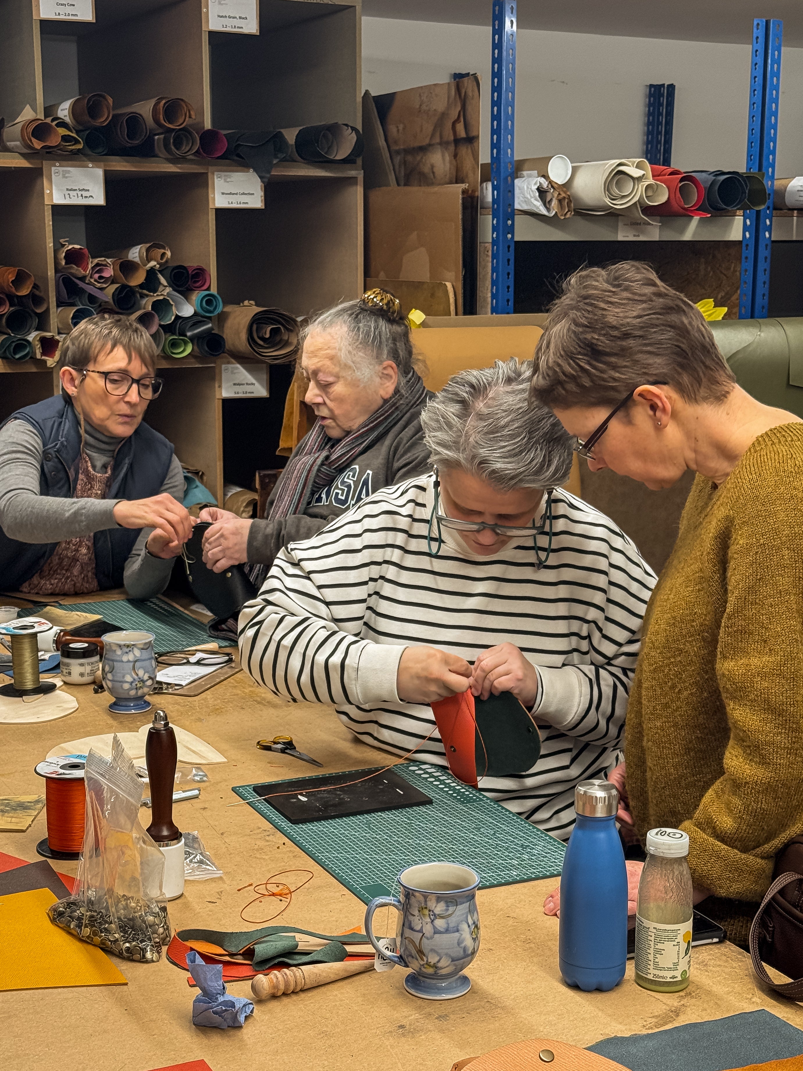 Four people working together at a table with various tools and materials in a workshop setting.
