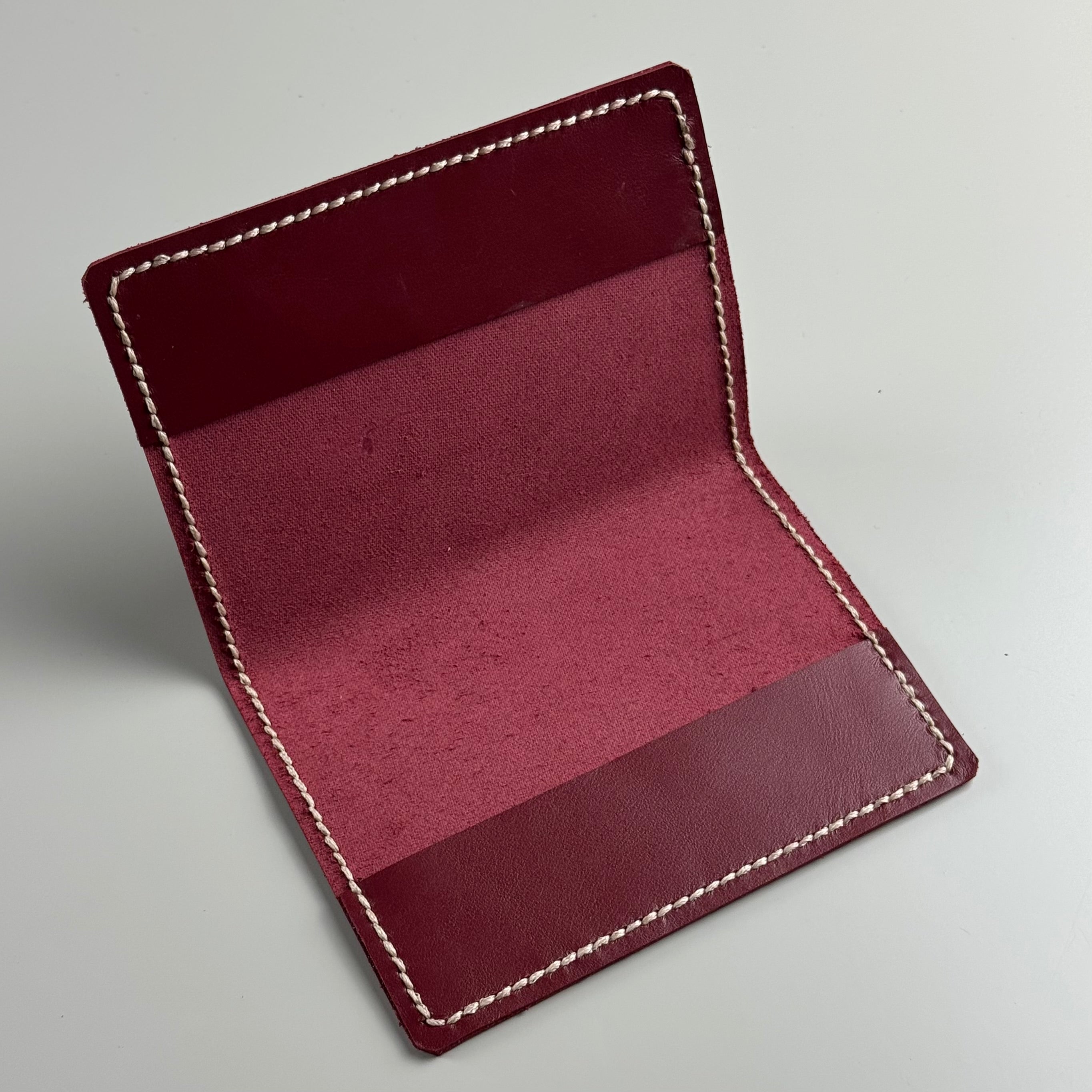 Maroon leather passportcover with white stitching on a light gray background