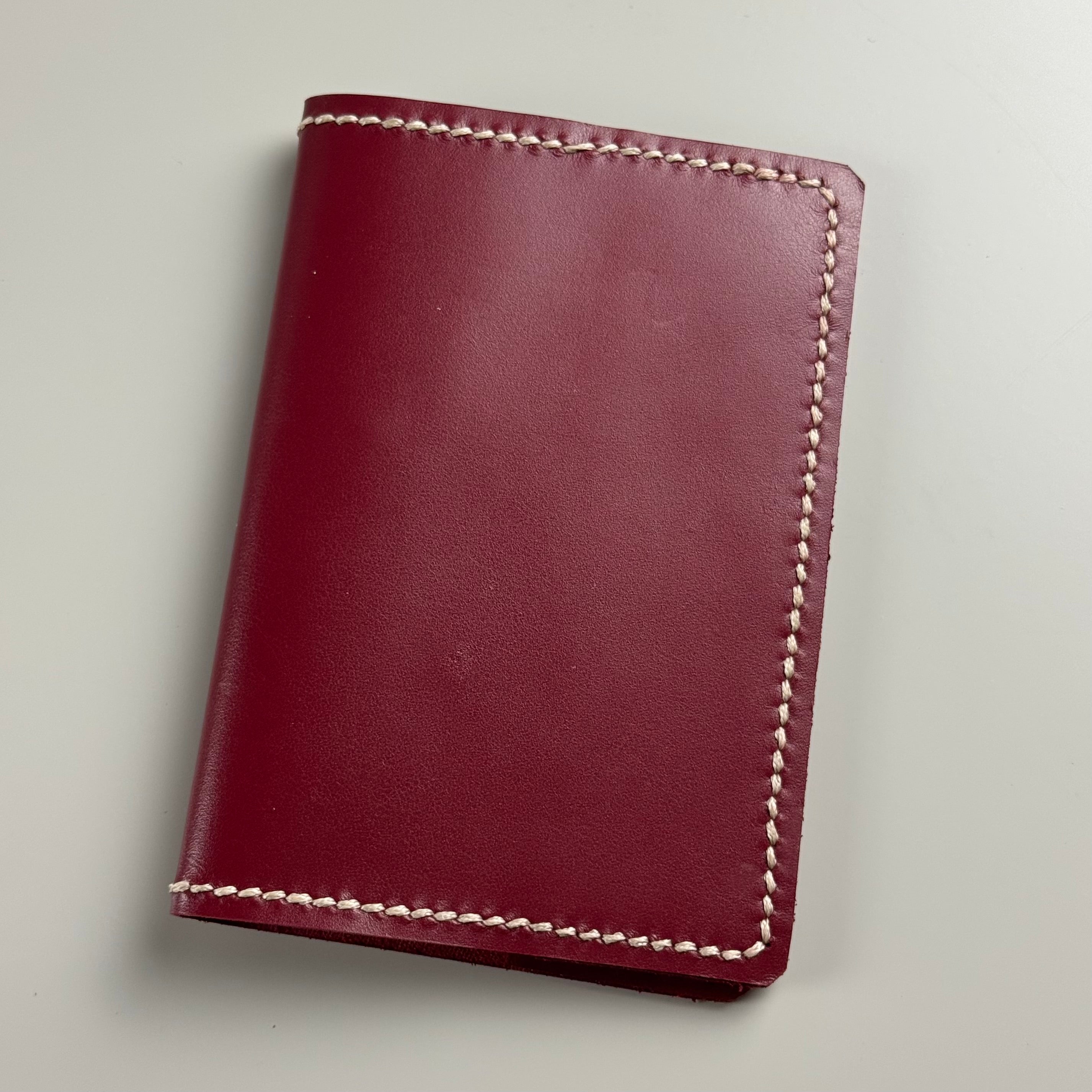 Maroon leather passport cover with white stitching on a light gray background