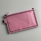 Pink leather purse with black stitching on a gray background