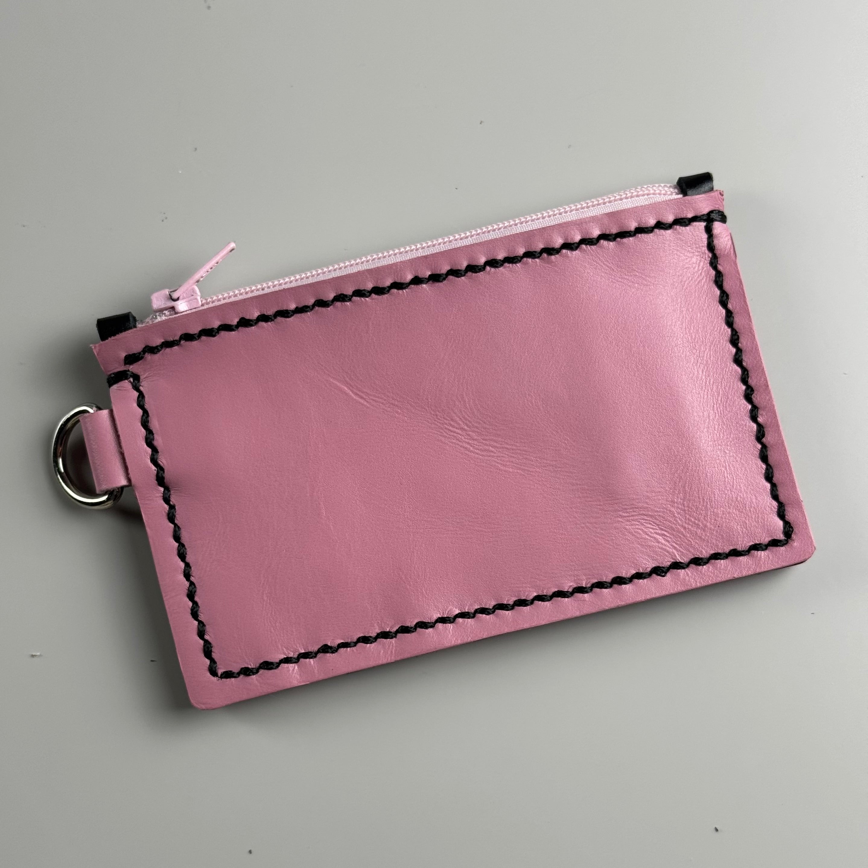 Pink leather purse with black stitching on a gray background