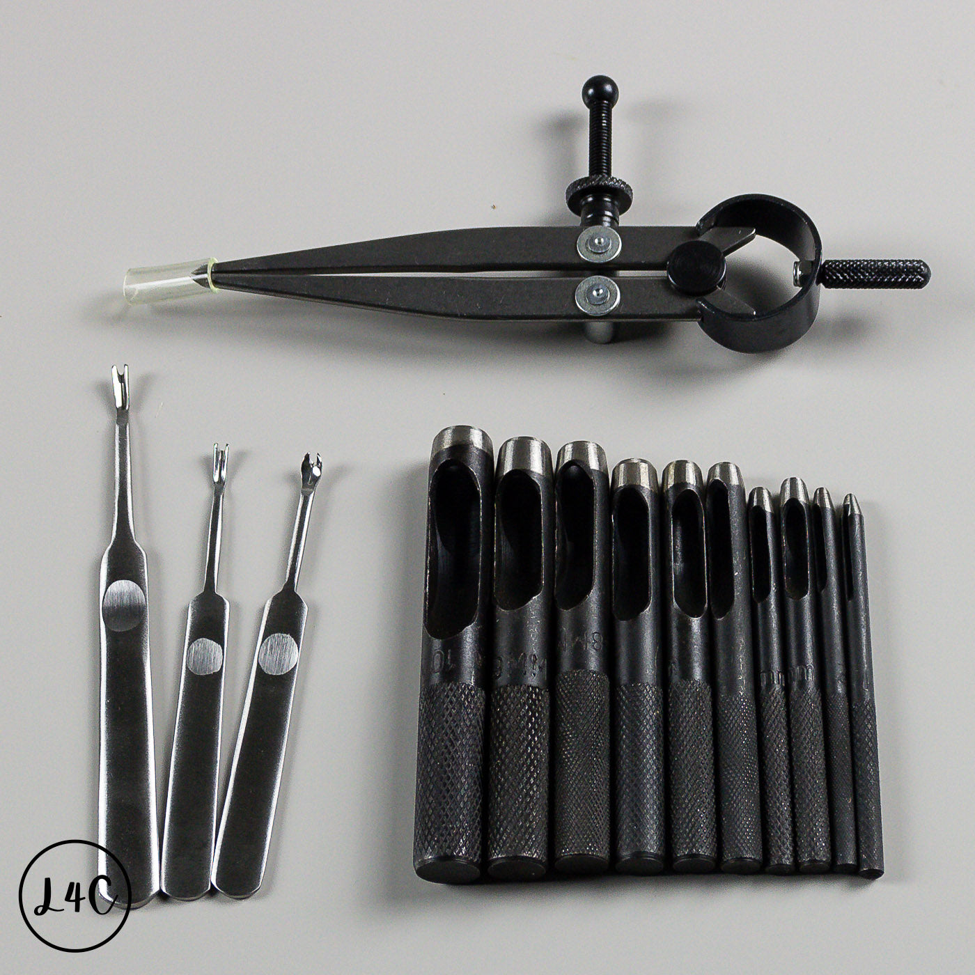 Set of black leather tools including wing dividers and hole punches on a gray background.