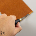 Hand using a rougher on a piece of brown leather.