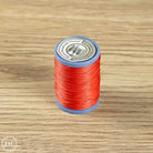 A spool of bright red sewing thread standing upright on a light brown wood-grain surface. 