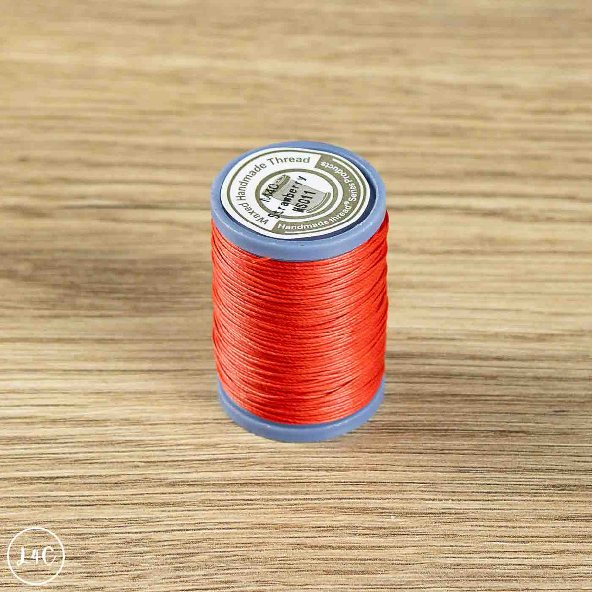A spool of bright red sewing thread standing upright on a light brown wood-grain surface. 