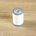 A spool of white sewing thread with blue plastic ends and a white label, placed on a light brown wood-grain surface.