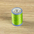 A spool of bright lime green sewing thread on a blue plastic core, placed on a light wood grain surface. The top label reads 'MAQ Traveller Sewing Thread' and 'K5027'.