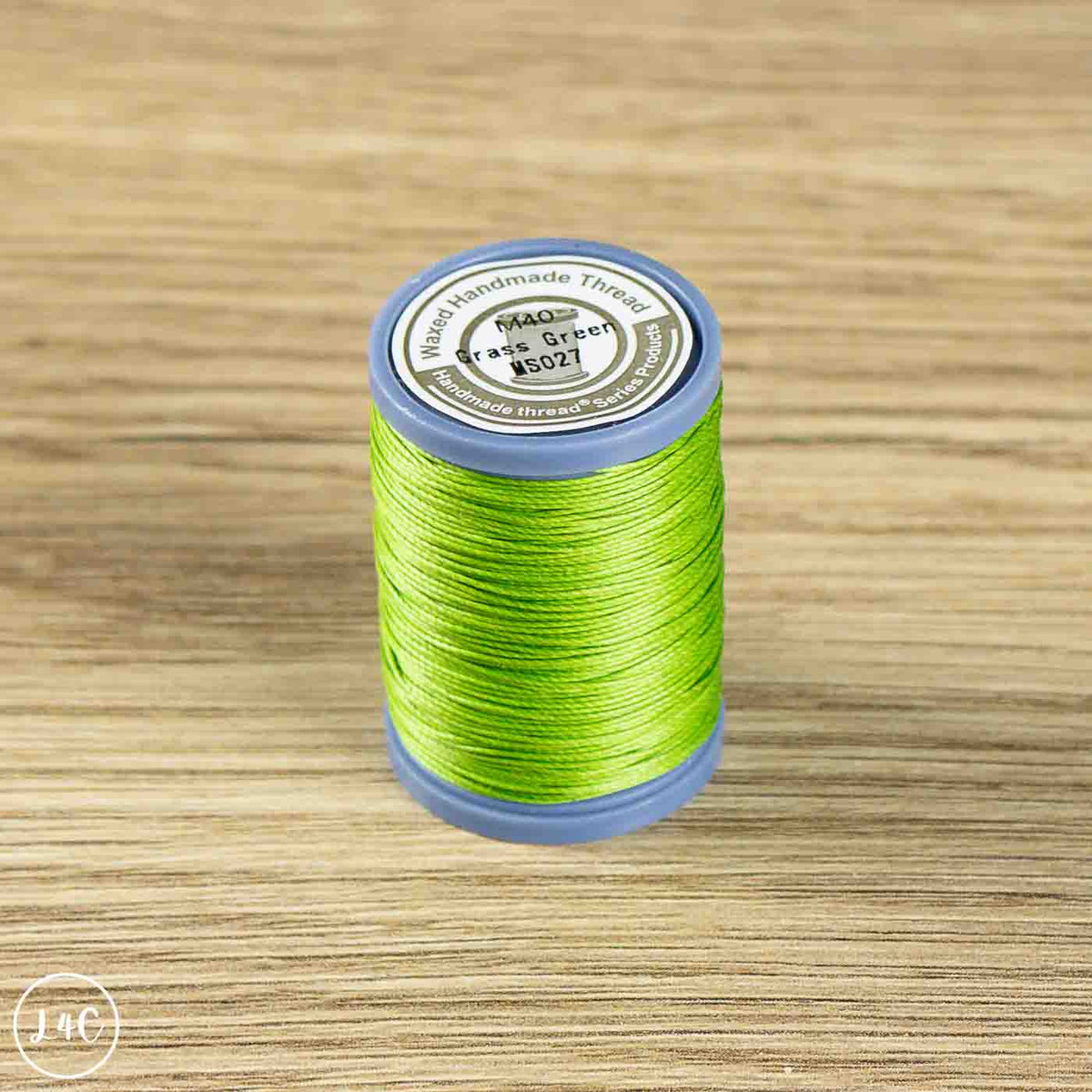 A spool of bright lime green sewing thread on a blue plastic core, placed on a light wood grain surface. The top label reads 'MAQ Traveller Sewing Thread' and 'K5027'.