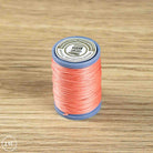 A spool of coral pink sewing thread on a blue plastic core, placed on a light brown wooden surface. 