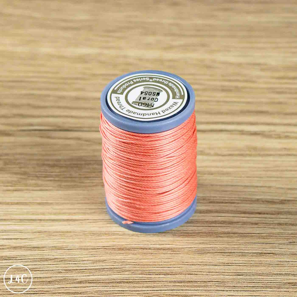 A spool of coral pink sewing thread on a blue plastic core, placed on a light brown wooden surface. 