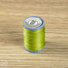 A spool of bright lime green sewing thread standing upright on a light brown wood-grain surface. The spool has a blue-gray plastic base and a white circular label on top with black text.