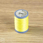 A spool of bright yellow sewing thread with blue plastic ends and a white label, placed on a light brown wood-grain surface.