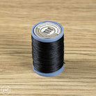 A spool of black waxed thread standing upright on a light brown wood-grain surface.
