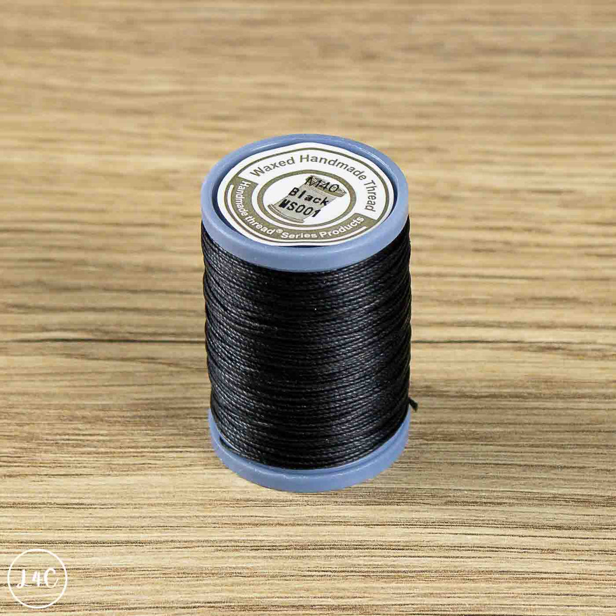 A spool of black waxed thread standing upright on a light brown wood-grain surface.