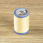 A spool of light beige sewing thread wound on a blue plastic core, placed on a light brown wood-grain surface. 