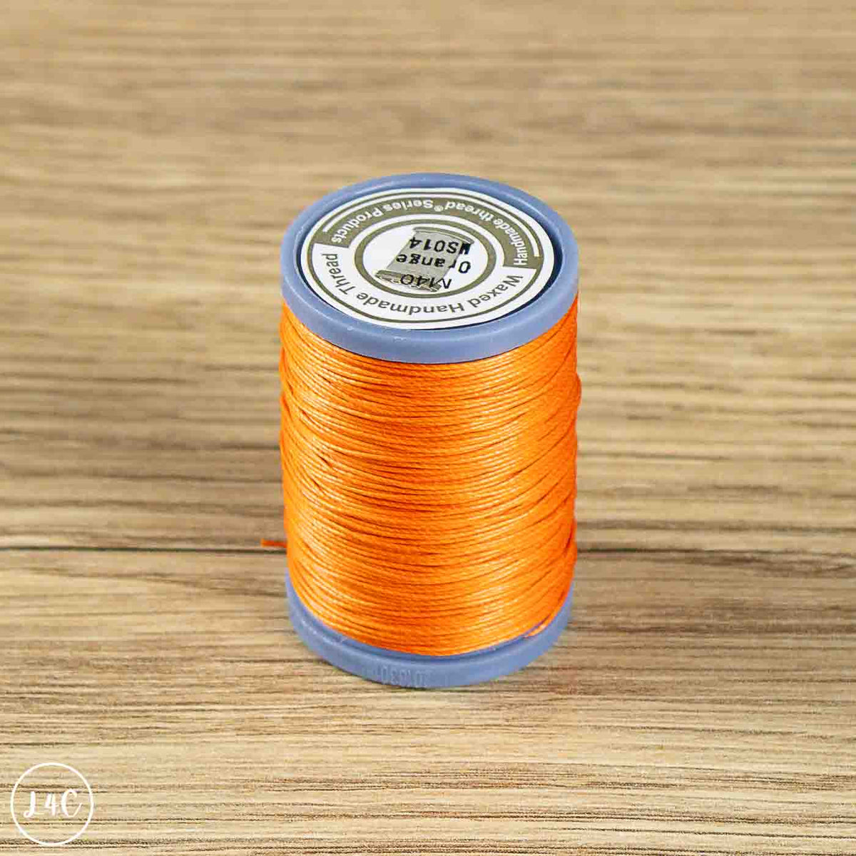 A spool of bright orange thread on a blue plastic core, set against a light brown wood grain background. 
