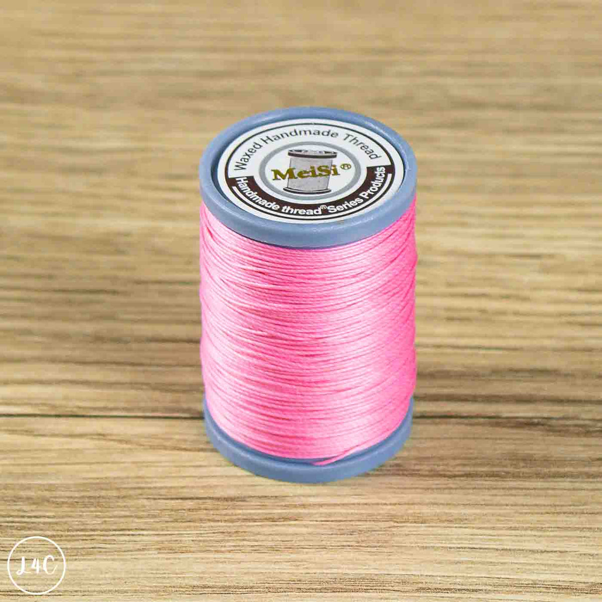 A spool of bright pink MelSi brand sewing thread on a gray spool, set on a light brown wooden surface.