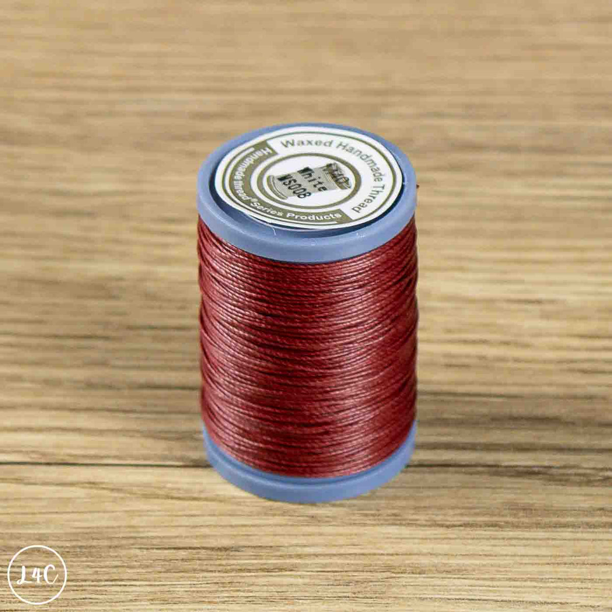 A spool of red waxed cotton embroidery thread on a light brown wooden surface. The spool has a blue plastic base and a white top label with black text.