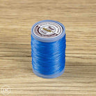A spool of blue waxed cotton embroidery thread standing upright on a light brown wood-grain surface. 