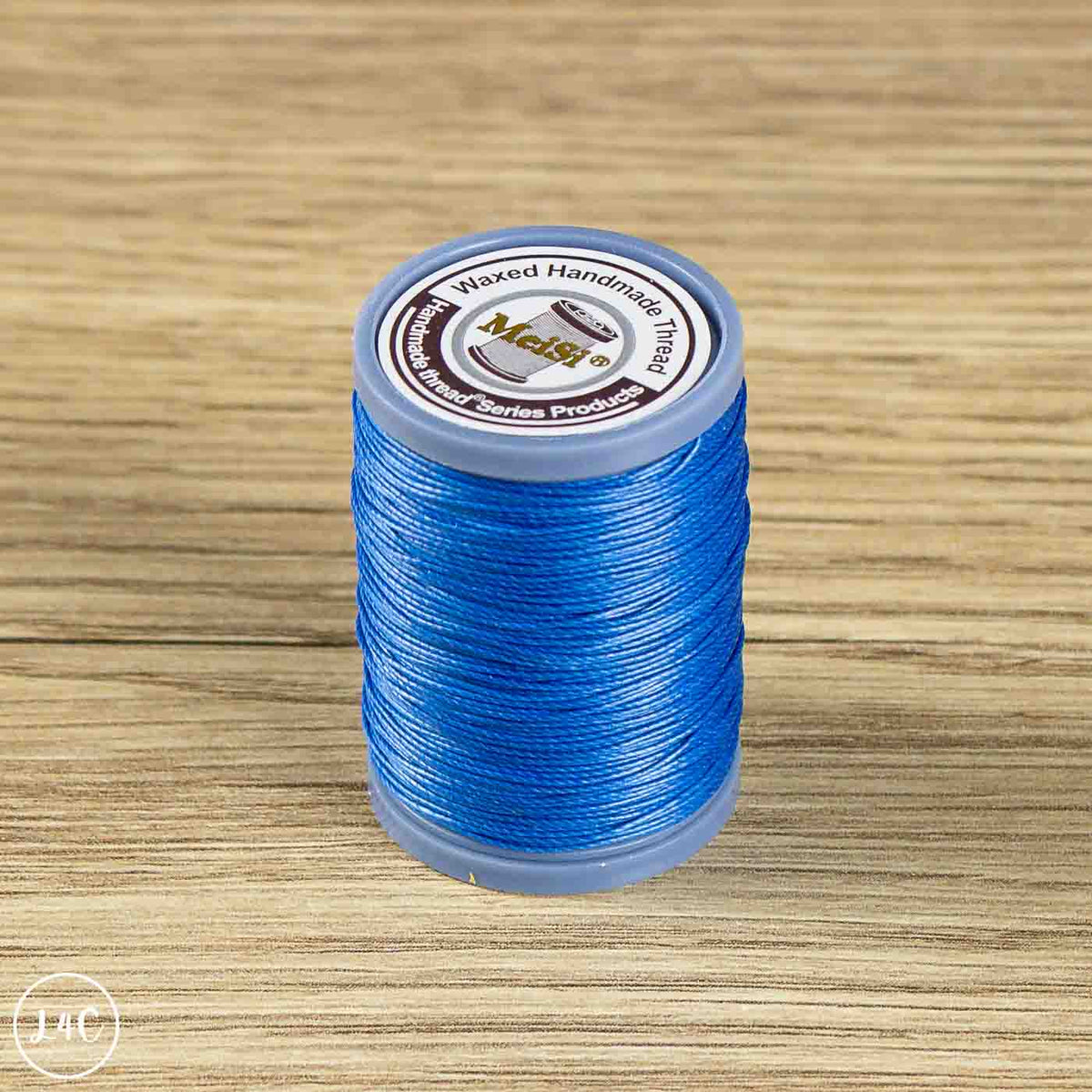 A spool of blue waxed cotton embroidery thread standing upright on a light brown wood-grain surface. 