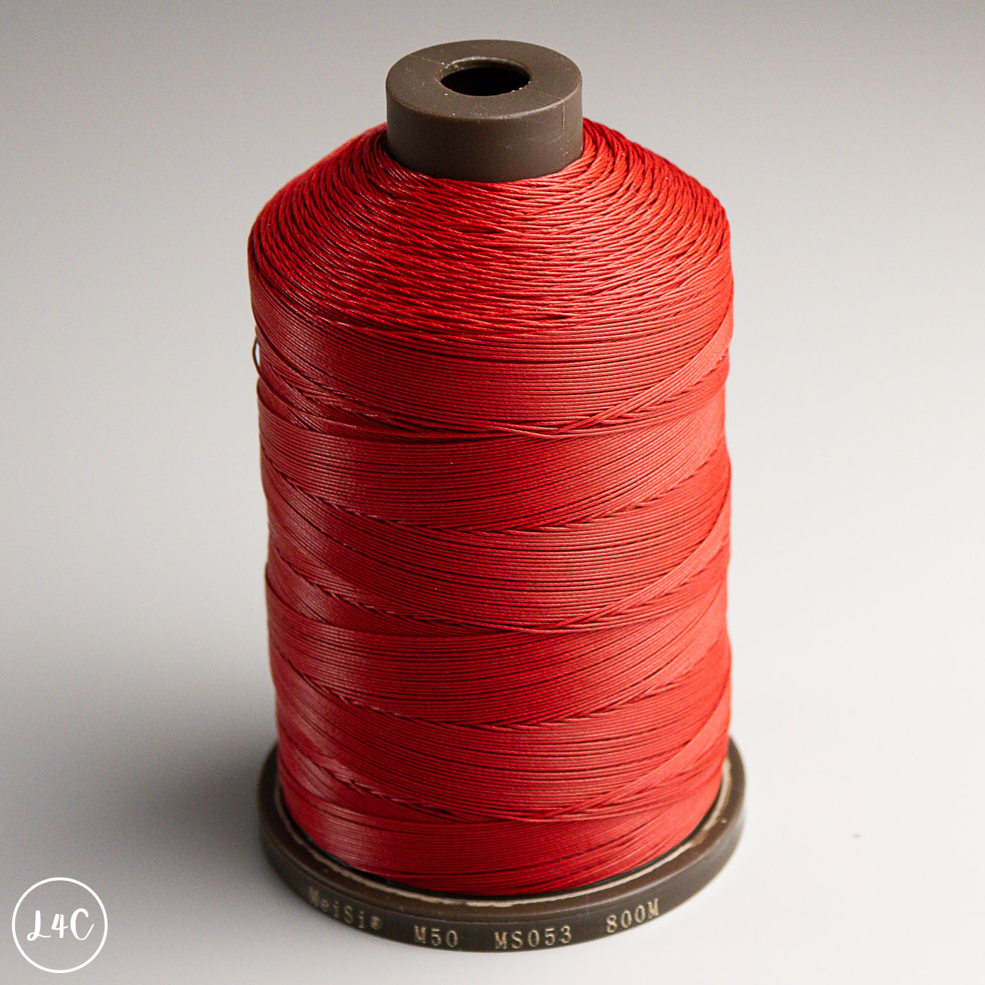 Spool of red MeiSi Waxed Linen Thread on a gray background
